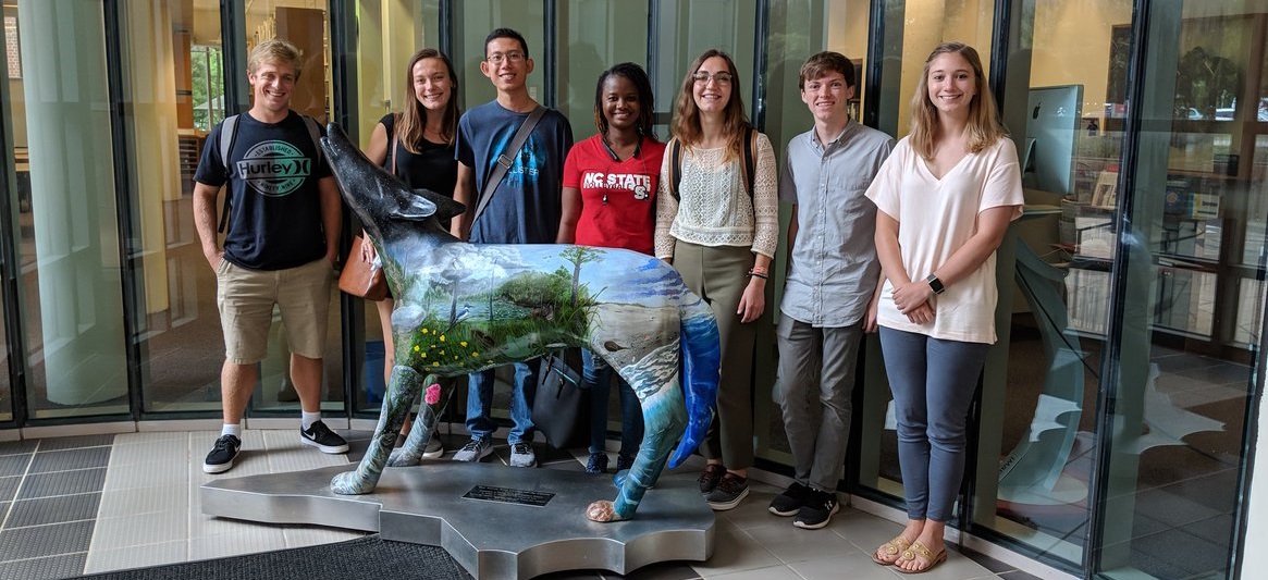 Students standing in front of statue of a wolf